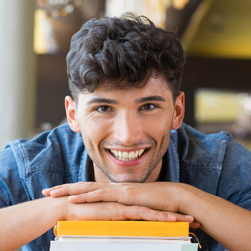 Smiling student resting on a pile of books Smiling student resting on a pile of books
